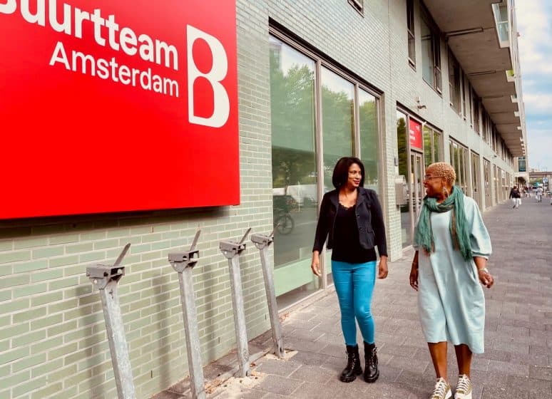 Twee vrouwen lopen langs het gebouw van Buurtteam Amsterdam, waar het spreekuur is